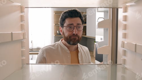 Preview: Hungry Caucasian bachelor man looking for food in empty fridge finding no meal products feeling sad