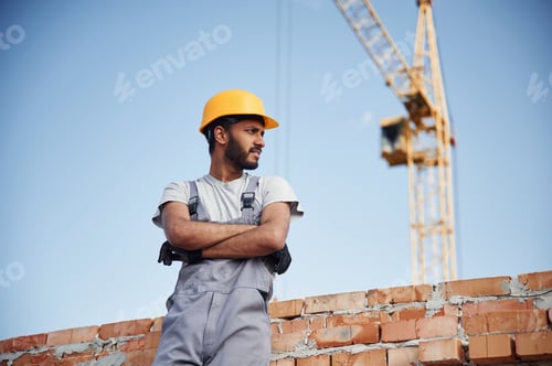 Preview: Standing against crane and blue sky. Handsome Indian man is on the construction site