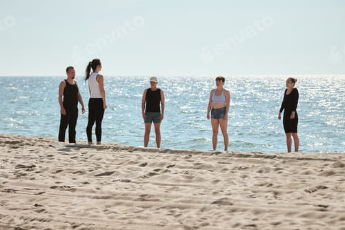 Preview: Group of adults practicing yoga on Baltic Sea sandy beach at sunrise