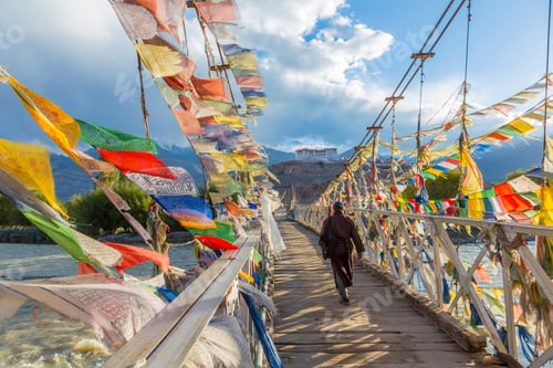 Preview: Rear view of man walking across bridge decorated with colourful prayer flags.