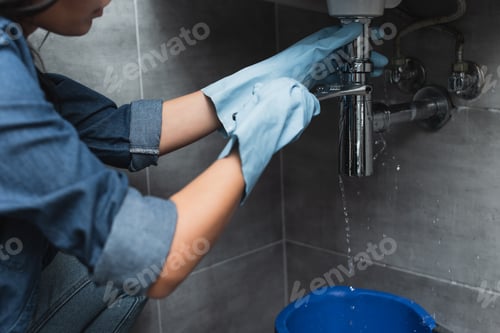 Preview: Partial view of woman in blue rubber gloves repairing pipe with wrench