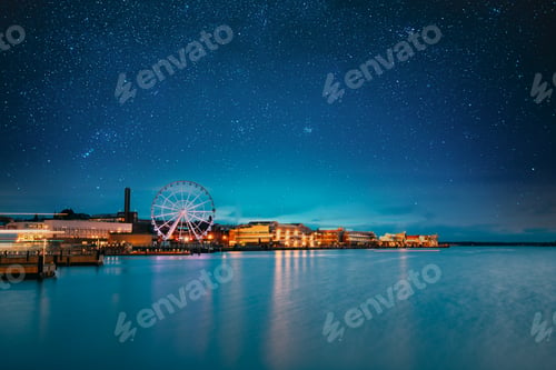 Preview: Helsinki, Finland. Bright Blue Starry Sky Above Embankment With Ferris Wheel In Evening Night
