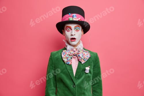 Preview: Shocked embarrassed hatter stares at camera with bugged eyes dressed in green jacket bowtie and big