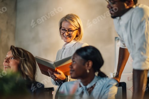 Vista previa: Senior businesswoman with textbook on meeting with interracial team.