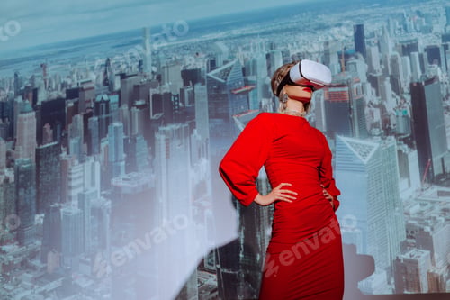 Preview: low angle view of stylish woman with hands on hips in red dress and virtual reality headset on city