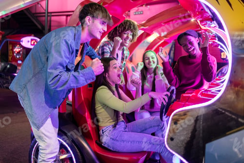Preview: group of multiracial friends having fun playing video arcade and dancing in a night room