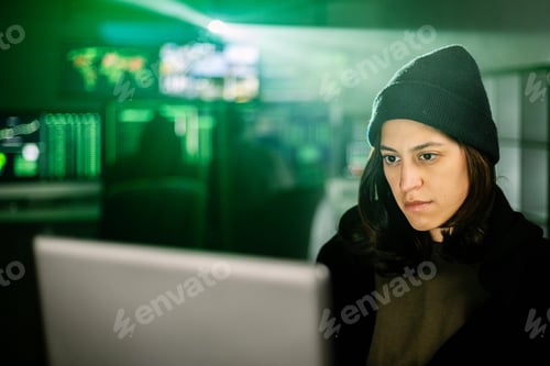 Preview: Female young hacker working on computer in dark room programming code