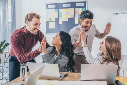 Preview: happy multicultural businesswomen and businessmen giving high five in office