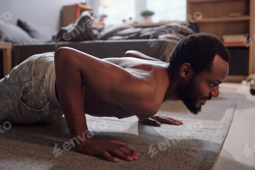 Preview: Young active man doing press-ups on the floor of bedroom