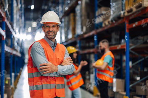 Preview: Warehouse manager smiling with crossed arms in busy warehouse