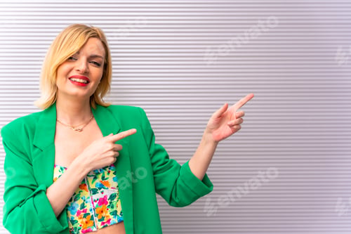 Preview: Portrait of a pretty blonde model in a green jacket pointing to the right, copy space