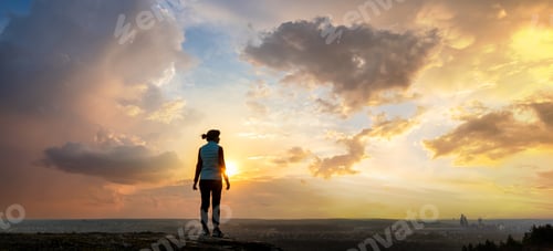 Preview: Silhouette of a woman hiker standing alone enjoying sunset outdoors.