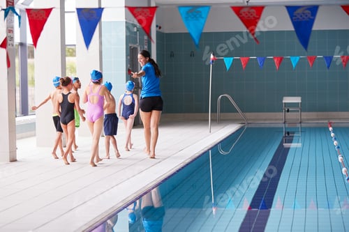 Preview: Female Coach Walks Children In Swimming Class Along Edge Of Indoor Pool