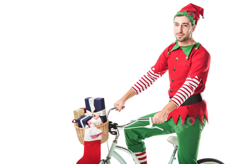 Preview: man in christmas elf costume looking at camera and riding bike with basket full of presents isolated