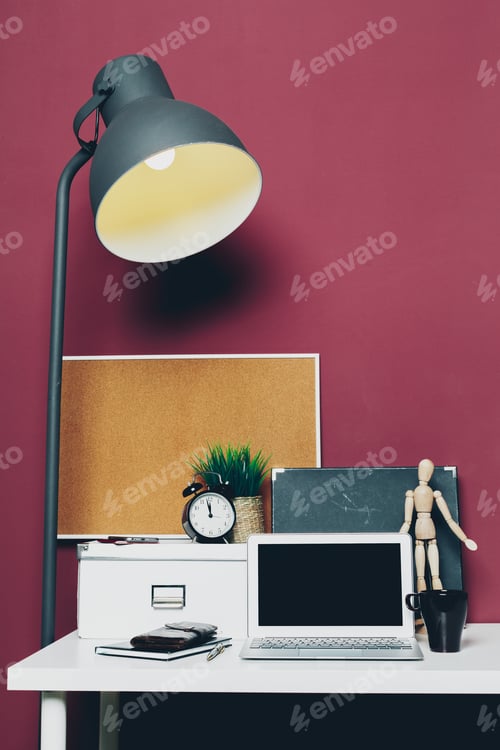 Preview: Different stationery at home office of a woman with laptop against dark pink wall