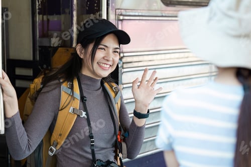 Preview: Young Female Traveler with Backpack and Camera Greeting Friend at Train Station, Ready for Adventure