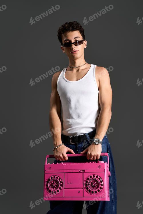 Preview: Stylish teenager in a tank top poses confidently with a pink boombox on a grey backdrop