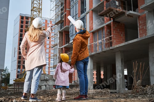 Preview: Family with child standing outdoors near building under construction.