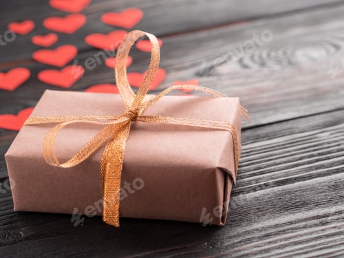 Preview: gift box with ribbon and lots of little red hearts on wooden texture dark background, side view