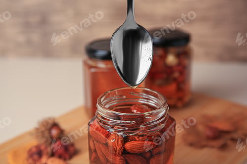Preview: Honey dripping from spoon into glass jar with nuts, closeup