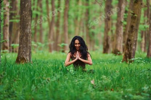 Preview: Positive brunette in casual clothes meditating in the forest at daytime