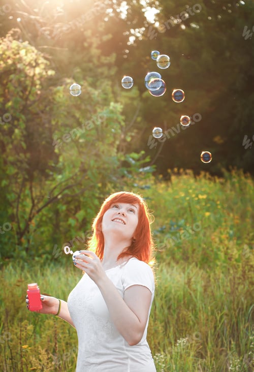 Preview: Dreamy young red haired woman with soap bubbles. Happy girl in nature in the sun. A symbol of