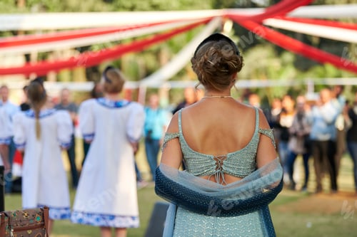 Preview: Back view of attractive woman in backless green dress looks at dancing performance at festival