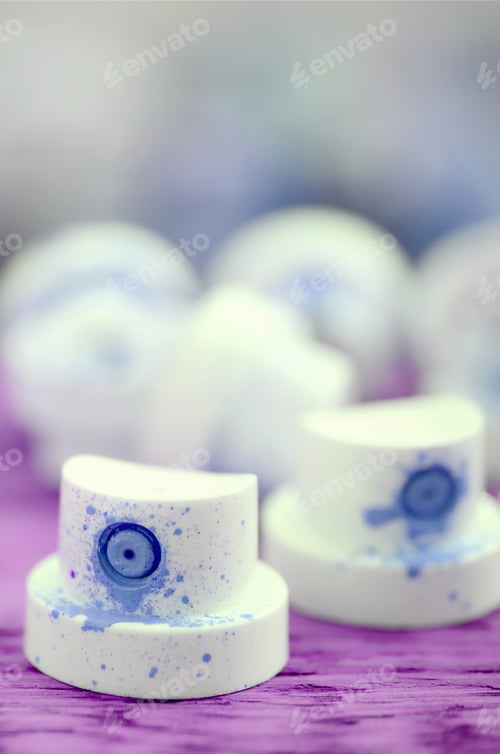 Preview: The soiled blue nozzles from the paint sprayer lies on a purple plank on a background