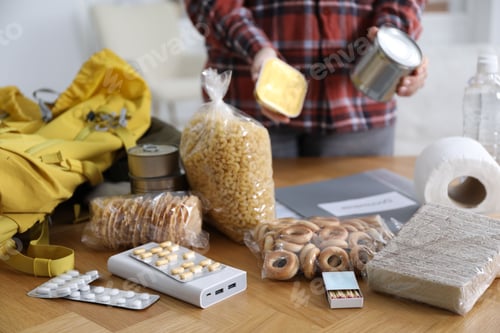 Preview: Survival kit. Woman packing different emergency supplies at wooden table indoors, selective focus