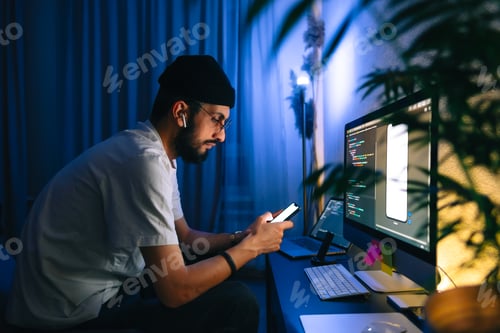 Preview: Young man mobile developer writes program code on a computer and check app in smartphone