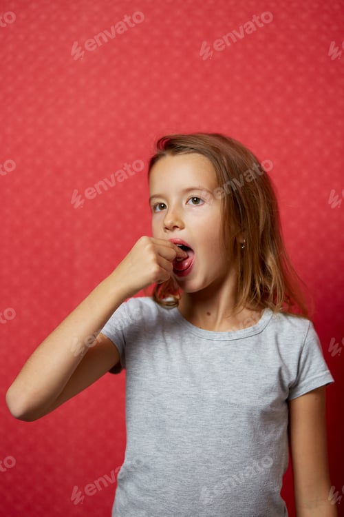 Preview: Portrait happy girl take capsule pill on her tongue on red background