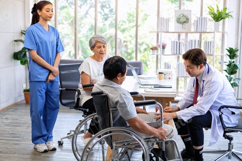 Preview: Senior couple male on wheel chair having consultations with doctor for knee problems at clinic