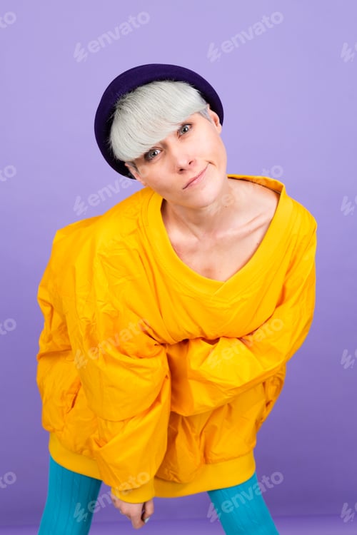 Preview: Stylish european woman on purple background posing wearing yellow large jacket and hat