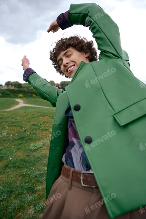 Preview: Young man enjoying a refreshing walk outdoors wearing a vibrant green coat on a sunny day