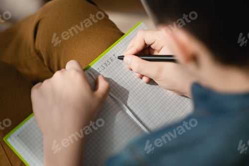 Preview: selective focus of schoolboy writing in copy book while making schoolwork at home