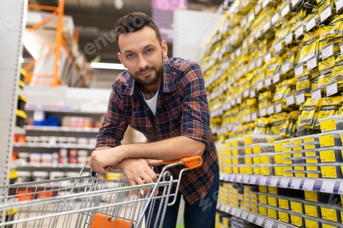 Preview: shopper in a hardware store looking at the camera bending over a trolley for goods, Concept of