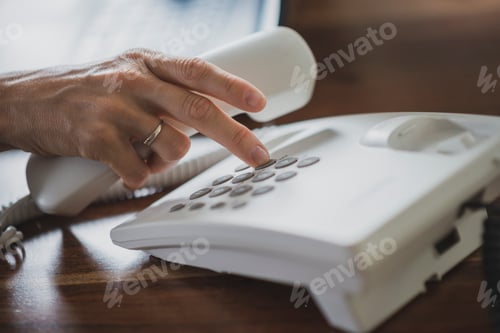 Preview: Female hand holding white landline telephone receiver dialing a phone number