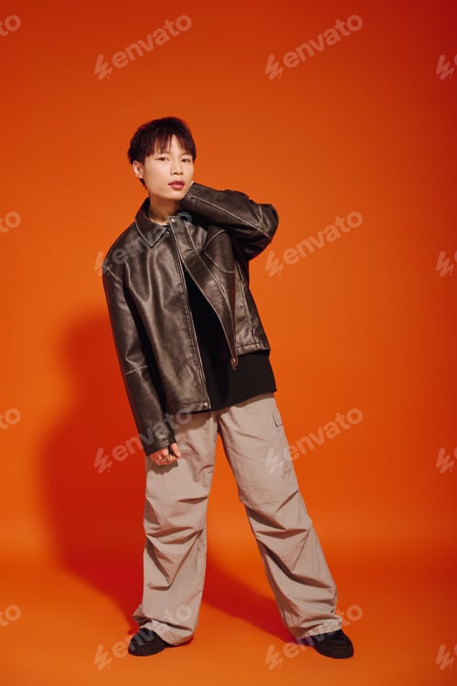 Preview: Stylish young man showcasing modern fashion against a vibrant orange backdrop