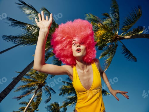 Preview: A woman with a pink wig posing among palm trees, showing joy and confidence in an outdoor setting