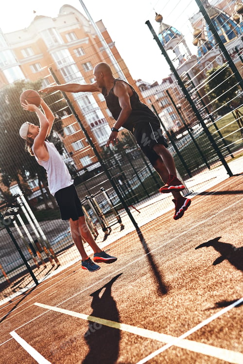 Preview: Playing hard. Two young men in sports clothing playing basketball while spending time outdoors
