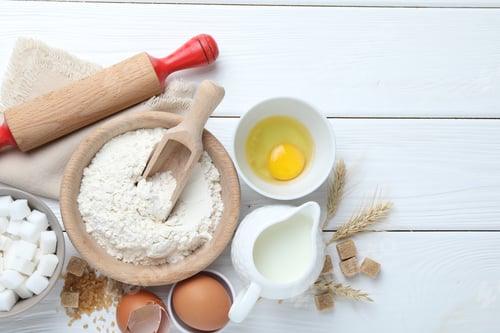 Preview: Rolling pin and ingredients for dough on white wooden table, flat lay. Space for text