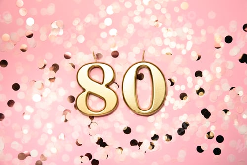 Vista previa: Vela dorada número 80 de celebración de cumpleaños de ochenta sobre fondo festivo.