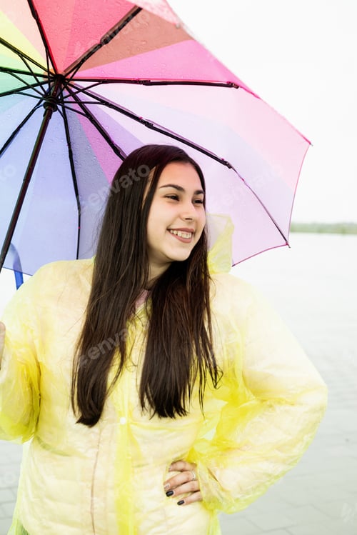 Preview: Beautiful brunette woman holding colorful umbrella out in the rain