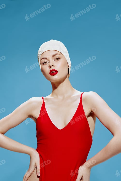 Preview: An arrogant female model in a bathing cap in a red swimsuit holds her hands at her waist, looking at