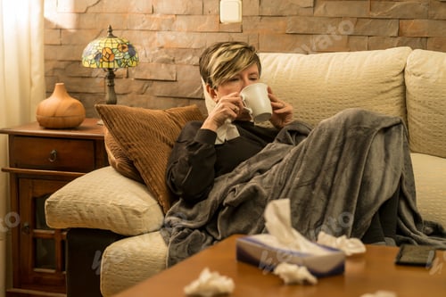 Preview: Woman drinking warm tea to help her with her cold, used tissues in the foreground