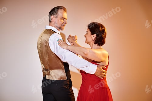Preview: Ballroom dance middle aged couple in red dress and suit dancing tango with yellow light on grey