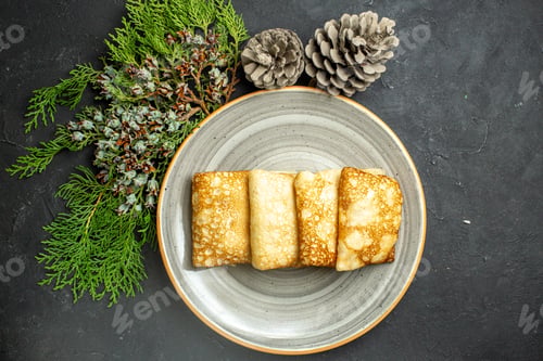 Preview: Horizontal view of delicious meat-filled pancakes on a white plate and conifer cone on black