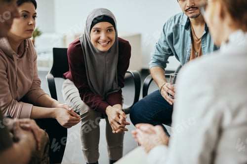 Preview: Happy Muslim woman and attenders of group therapy talking with their psychotherapist.