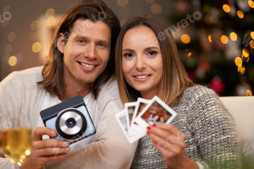 Preview: Beautiful couple celebrating Christmas at home and taking instant pictures