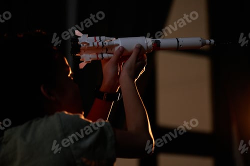 Preview: Joyful boy having fun playing with toy space rocket at night